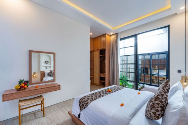 Serene Balinese bedroom with wooden vanity, tropical bed, large glass doors, and potted plants.